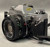 Three-quarter view of Canon AE-1 body with attached FD 50mm lens on gray background