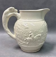 Front view of white ceramic pitcher with relief of riders and horses, dog-shaped handle visible