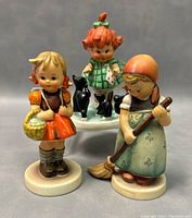 Front view of three Hummel figurines showing detailed hand painting and size proportions.