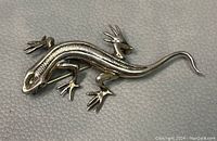 Front view of vintage silver-tone lizard brooch showing detailed body and legs with long tail.