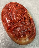 Front view of red stone pendant showing detailed dragon and character carving on the surface.