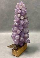 Front-angle view of the amethyst grape cluster sculpture showing the clustered polished stone grapes and wooden base with metal leaves