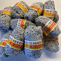Seventeen balls of pale grey and cream twisted wool yarn with original labels stacked together.