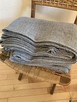 Folded wool crepe fabric on a chair showing full yardage stacking and grey color.