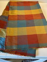 Folded multicolor checked silk fabric on a white table, showing the overall pattern and sheen.