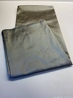 Folded piece of smooth silk fabric in muted grey with pale green hints, showing overall texture and color.