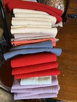Stack of 24 folded wool fabric pieces in colors including red, cream, orange, blue-gray, and purple laid out on a wooden surface.