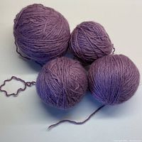 Four balls of 100% wool yarn in soft lavender, prewound and placed together on a white surface.