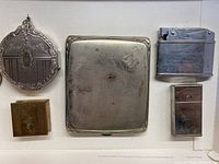 Overview of 4 metal containers and 2 lighters laid out on white surface, showing condition and details