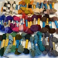 Full view of assortment of 60 skeins of wool tapestry yarn in various colors including white, cream, oranges, browns, reds, purples, blues, greens and grays.