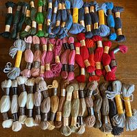 Wide top-down view of 60 skeins of wool tapestry yarn arranged by color groups including greens, blues, pinks, reds, browns, and neutrals.
