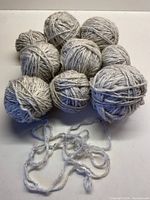 Eight pale grey wool yarn balls with black flecks, arranged in a cluster with one showing loose strands.