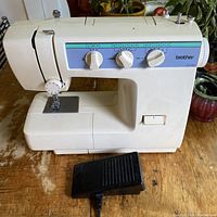 Front and left side view showing machine body with open arm, needle plate, and foot pedal on wooden surface.