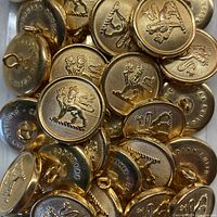 Close-up photo showing multiple brass buttons piled together, displaying the Royal Lion motif on the front faces and securing shanks on the back.