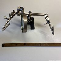 Front view of the Excel soldering station showing magnifier and clamps extended with a wooden ruler for size reference.