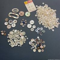 Wide view of assorted vintage mother of pearl buttons separated in groups by size and color. Includes card with 6 white buttons, oval buckle buttons, and various round buttons.