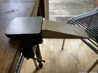 Cast iron clamp attached to a wooden surface with wooden bench pin inserted, showing the tool's side profile and fitment.