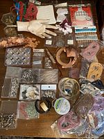 Wide shot of assorted jewelry supplies including colored cords, copper pieces, beads in containers, jump rings, and a mannequin hand