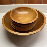 Stacked view of one large bowl with four smaller bowls nested inside, showing smooth finish and wood grain.