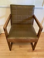 Full front view of the chair showing olive green pleather upholstery and teak wood frame.