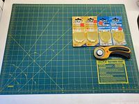 Rotary mat with grid and measurement lines, rotary cutter, and 4 unopened blades placed on mat
