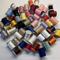 Photo showing a large assortment of over 50 thread spools in various colors, mostly polyester with some cotton, including unopened and opened spools.