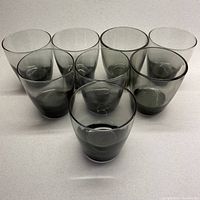 Eight smoky grey lowball glasses arranged in two rows, showing color gradient from base to rim.