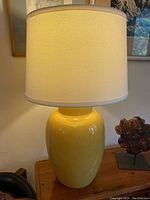 Front view of vintage yellow ceramic lamp with cream shade on wooden table.