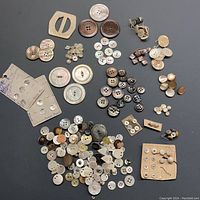 Over 100 assorted vintage mother of pearl buttons laid out loosely, displaying a wide variety of sizes, shapes, and colors.
