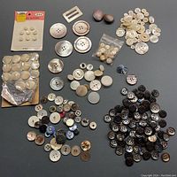 Photo showing large assortment of mother of pearl buttons in many sizes, shapes and colors including some carded buttons and buckle.