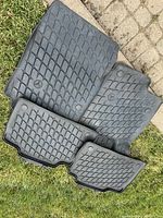 Four-piece set of black rubber winter floor mats for Mercedes Benz GLA250, shown laid out on grass and pavement, displaying diamond pattern and Mercedes logos.