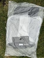 Set of new Porsche Macan floor mats sealed in a clear plastic bag laid on grass, showing distinctive diamond-quilt pattern and off-white coloring.