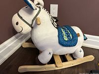 Side view of plush white rocking horse with wooden rockers, blue patterned saddle, and wooden handles.