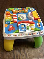 Top and partial side view of colorful plastic baby activity table with various interactive elements and alphabet letters on the border