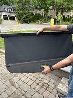 Photo showing the Mercedes-Benz GLC rear trunk cover held by a person outside, highlighting the black fabric cover with mounting frame ends.