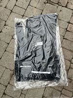 Photo of sealed black Mercedes-Benz AMG floor mat branded packaging lying on stone pavement.