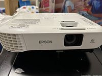 Front view of Epson projector showing lens, ventilation grilles and brand label.