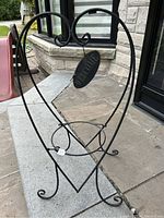 Black metal garden flower stand in heart shape with a 'Welcome' oval sign, standing on a stone patio in front of a building.