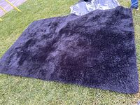 Top view of a large black shaggy mat laid on grass, showing overall size and texture.