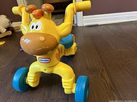 Front angle photo of the yellow giraffe Little Tikes ride-on toy showing its four blue wheels and yellow handlebars.