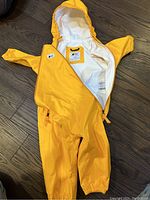 Yellow infant raincoat laid out on floor showing front side with hood, full zipper, elastic wrists and ankles.