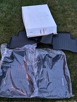 Four new floor mats for Mercedes-Benz GLS450, two rubber mats and two carpet mats still wrapped in plastic, with original box on grass.