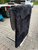 Photo of black shag carpet hanging vertically to show pile texture and thickness, outdoor setting.