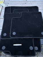 Four black carpet floor mats for Mercedes-Benz GLC SUV, one with logo plaque and circular securing grommets visible.