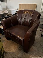 Brown leather office sofa chair photographed frontally on a concrete floor showing white stitching detail, cushioned seat, and backrest.
