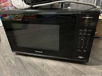 Front view of Panasonic black microwave oven showing control panel with numeric keypad and different cooking mode buttons.