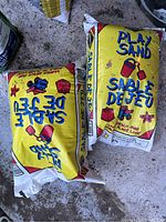 Two bags of Play Sand labeled 'Sable De Jeu' photographed on a concrete floor.