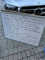 Framed writable poster board with handwritten notes involving dates, codes, and scheduling information.