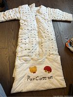 Baby sleeping bag laid flat showing full length with zipper and matching pillow featuring bear and mushroom decorations and PurCotton logo.