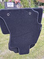 Photo of front side of dark gray carpet mat with reinforced edges and grommets, showing contour shape designed for vehicle floor.